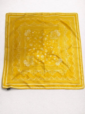Gul bandana med paisleymönster - Snygg gul bandana med klassiskt paisleymönster i vitt. Perfekt att ha som accessoar runt halsen, i håret eller på väskan. Tunt och mjukt material som är lätt att vika och styla på olika sätt.