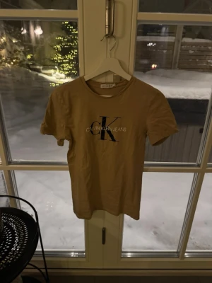 Beige Calvin Klein t-shirt xs - Snygg beige t-shirt från Calvin Klein Jeans med stor CK-logga tryckt på bröstet. Klassisk rund halsringning och korta ärmar. Perfekt basic-plagg med stilren design som funkar till allt. Tillverkad i mjuk bomull för skön känsla.