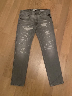 Replay Anbass grå slim jeans herr - Säljer ett par Replay Anbass slim fit jeans i grå tvätt med slitna detaljer framtill och baktill. Jeansen har klassisk femficksmodell och har raka ben. Endast använda ett fåtal gånger. Köpare står för frakt.