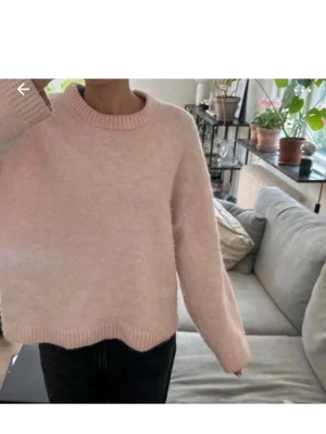 Ljusrosa stickad tröja med rund hals - Mysig ljusrosa stickad tröja med rund hals och ribbade muddar vid ärmslut och nederkant. Tröjan har en loose passform och långa ärmar, perfekt för att hålla sig varm under kyliga dagar. Enkel och stilren design som är lätt att matcha med olika outfits.