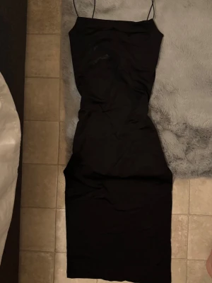 Svart långklänning från Zara - Säljer en svart långklänning från Zara med tunna axelband och figurnära passform. Klänningen har en enkel och stilren design som gör den lätt att styla. Materialet känns mjukt och följsamt mot kroppen.