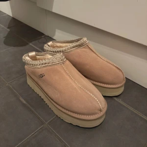 Beige UGG platå boots - Säljer ett par beige UGG boots med platåsula och rund tå. Skorna är i mjuk mocka med stickad detalj runt öppningen och har en rejäl, räfflad sula för extra grepp. Perfekta för kalla dagar och riktigt sköna att ha på sig.