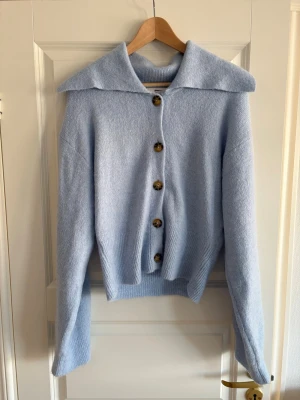 Ljusblå stickad kofta från Gina Tricot M nyskick  - Superfin ljusblå stickad kofta från Gina Tricot med stora bruna knappar och bred krage. Koftan har lång ärm, ribbad nederkant och är perfekt för lager-på-lager. Mjuk och skön känsla, passar dig som gillar chill och stilren look.