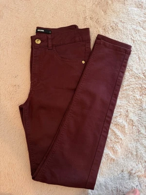Vinröda skinny jeans från Bik Bok - Snygga vinröda jeans från Bik Bok i skinny fit. Byxorna har klassisk femficksdesign, guldiga detaljer vid knappar och nitar samt smal passform. Perfekta att matcha med sneakers eller boots för en cool look.
