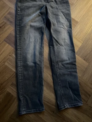 Levi's 501 mörkgrå jeans straight fit - Säljer ett par Levi's 501 jeans i mörkgrå tvätt med klassisk straight fit. Jeansen har fem fickor, synliga sömmar och den ikoniska Levi's-detaljen på bakfickorna. Materialet är slitstarkt jeans och passformen är normal. Perfekt för dig som gillar tidlös stil.