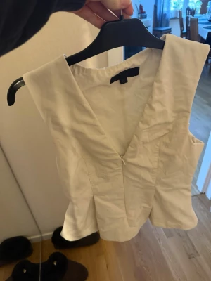 Vit v-ringad korsett från Zara - Säljer en stilren vit korsett från Zara med v-ringning och dragkedja framtill. Toppen är ärmlös och har en lätt figurnära passform som ger en snygg siluett. Perfekt att styla med jeans eller kjol för en clean look.