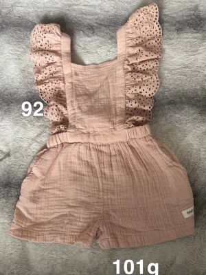 Rosa byxdress med volangärmar - Supersöt rosa byxdress med broderade volangärmar och elastisk midja. Perfekt för varma dagar och ger en gullig look med sina detaljerade spetsvolanger på axlarna.🌸 Oanvänd. Storlek 92