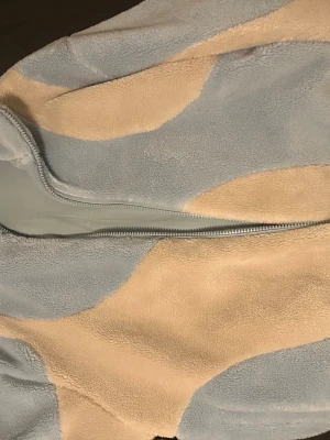 Blå och beige teddyjacka från YoungLA - Säljer en oversized teddyjacka från YoungLA i storlek M. Jackan har ett unikt mönster i ljusblått och beige, är tillverkad i mjuk fleece och har dragkedja framtill. Perfekt för dig som gillar en chill och trendig look.