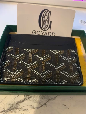 Goy4ard svart mönstrad plånbok - Säljer en stilren svart plånbok från Goy4ard med det klassiska grafiska mönstret i vitt och brunt. Plånboken är tillverkad i skinn och har flera fack för kort. Perfekt för dig som vill ha något både snyggt och praktiskt i fickan.