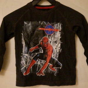 Svart långärmad Spiderman t-shirt - Cool svart långärmad t-shirt med stort Spiderman-tryck framtill.  Röd kontrastsöm längs ärmar och nederkant. Perfekt för dig som gillar superhjältar! Hund finns i hemmet. Kolla in mina andra annonser för samfrakt! 