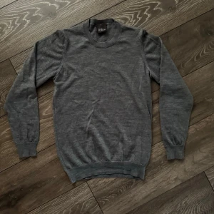 Grå stickad tröja från Oscar Jacobson - Säljer en stilren grå stickad tröja från Oscar Jacobson i storlek S. Tröjan har rund halsringning, ribbade muddar vid ärmslut och nederkant samt lång ärm. Perfekt för dig som gillar klassisk och enkel stil.