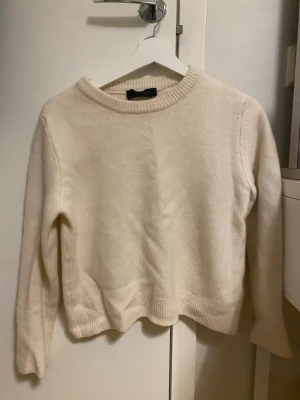 Beige stickad tröja med rund hals - Mysig beige stickad tröja med rund halsringning och ribbade muddar vid ärmslut och nederkant. Tröjan har en enkel och clean look, perfekt för lager på lager under kyliga dagar. Långärmad och i mjukt material som känns skönt mot huden.