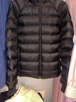 Svart pufferjacka Peak Performance S - Säljer en svart pufferjacka från Peak Performance i storlek S. Jackan har en quiltad design, dragkedja framtill och på fickorna samt diskret logga på bröstet. Perfekt för kalla dagar och riktigt snygg till alla outfits.