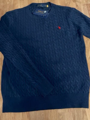 Ralph Lauren Stickad - Stilren och klassisk stickad tröja i marinblått från Ralph Lauren. Mjuk och bekväm kvalitet med tidlös design och diskret logga som lyfter outfiten. Perfekt för både vardag och mer uppklädda tillfällen
