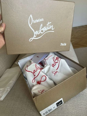 Grå mocka sneakers från Louboutin - Säljer ett par gråa sneakers från Christian Louboutin i mocka med ikoniska röda sulor och coola nitar på tån. Skorna har snörning och kommer med originalkartong, dustbags och extra skosnören. Perfekta för dig som vill sticka ut med exklusiv streetstyle. Storlek 42
