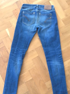 Dondup Blå skinny jeans med slitningar - Säljer ett par Dondup blå skinny jeans med slitningar och lagade detaljer på benen. Jeansen har klassisk femficksdesign, låg midja och kontrastsömmar. Materialet är jeans i bomull med lite stretch för skön passform.