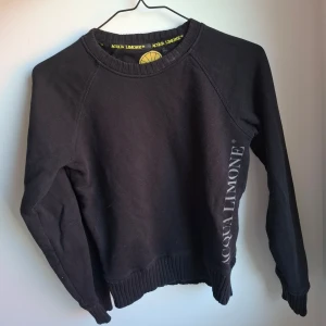 Svart sweatshirt Acqua Limone XXS - Svart sweatshirt från Acqua Limone i 100% bomull. Stor gul citronlogga på ryggen och tryckt logga på framsidan. Tröjan har rund hals, ribbade muddar och lång ärm. Perfekt för dig som gillar klassiska streetwear-vibes och vill sticka ut med en ikonisk logga. Jag kan inte garantera att den är äkta! Önskas fler bilder för att säkra om den är äkta är det bara att höra av sig. Tror detta är en äldre modell men är osäker 🖤
