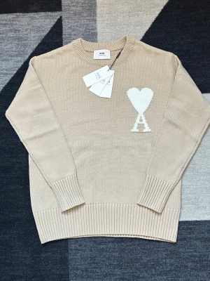Beige stickad tröja från Ami Paris  - Snygg beige stickad tröja från Ami Alexandre Mattiussi med ikonisk vit hjärtdetalj och bokstaven A på bröstet. Tröjan har rund hals, ribbade muddar och är långärmad. Helt ny och kommer med original paketet. Kan diskutera priset 