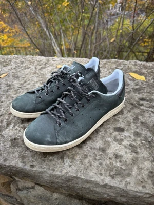 Adidas Stan Smith sneakers - Säljer ett par Adidas Stan Smith sneakers i svart skinn med vita detaljer och svartvita snören. Klassisk låg modell med perforerade hål på sidan och vit sula. Perfekta för dig som gillar tidlös streetstil och vill ha något som funkar året runt.