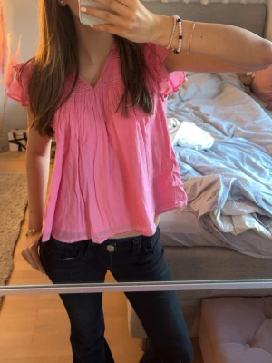 Rosa blus med volangärmar - Säljer en söt rosa blus med v-ringning och volangdetaljer på ärmarna. Blusen är luftig och har ett lätt rynkat tyg upptill samt spetsdetalj vid halsen. Perfekt till sommaren och ger en fräsch look till jeans eller kjol.