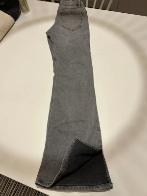  Lindex Freja Flare 152 cm - Säljer ett par gråa bootcut jeans från Lindex med snygga slitsar längst ner på benen och små pärldetaljer vid fickorna. Jeansen har klassisk femficksdesign och är tillverkade i mjukt jeansmaterial. Perfekta för dig som vill ha en cool och trendig look.