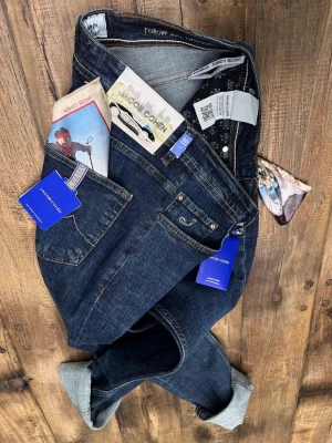 Mörkblå jeans från Jacob Cohën - Säljer ett par mörkblå jeans från Jacob Cohën med klassisk femficksdesign och snygga kontrastsömmar. Jeansen har ett coolt patch med bilmotiv bak och kommer med en färgglad scarf i fickan. Perfekt passform och exklusiv känsla.