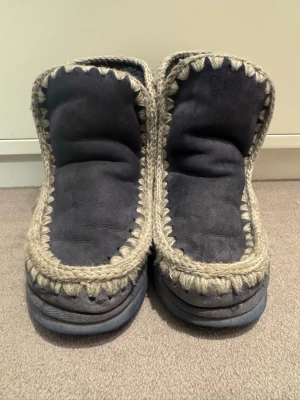 Mou boots i mörkgrå mocka - Säljer ett par boots från Mou i mörkgrå mocka med grov beige stickad kant runt hela skon. De har en platt sula i gummi och rund tå. Perfekta för kalla dagar med sin höga och mjuka design. Märket syns tydligt baktill och under sulan.