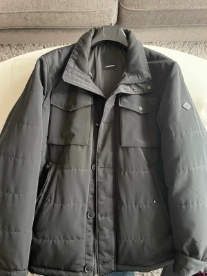 J.Lindeberg Bailey Field jacka XL – Primaloft – premium vinterjacka) - Stilren och varm vinterjacka från J.Lindeberg i storlek XL. Jackan är fylld med Primaloft, vilket ger mycket bra värme samtidigt som den är lätt och smidig.  ✔ Modern, minimalistisk design ✔ Perfekt för höst/vinter ✔ Hög kvalitet & premiumkänsla ✔ Flera fickor med knapp/dragkedja ✔ Färg: mörkgrå/svart  Använd men i mycket gott skick, inga större skador eller defekter. Passar både till vardag och mer uppklädda outfits.  Nypris ca 3 500–4 000 kr. Skickas alltid snabbt vid smidig affär.