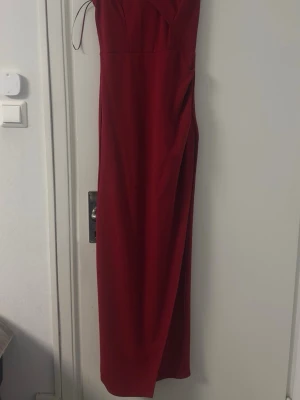 Röd långklänning med slits - Säljer en elegant röd långklänning som använts en gång innan med snygg slits på sidan. Klänningen är axelbandslös och har en stilren, enkel design som ger en lyxig känsla. Perfekt för bal eller fest.