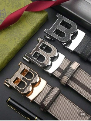 Burberry bälte - Snyggt bälte i beige med breda svarta ränder och ett stort B-format spänne i metall. Västen har en modern look med tydliga kontraster och detaljer i guld, silver eller svart. Materialet är troligtvis syntet eller polyester och designen känns lyxig och trendig.