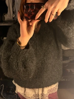 Mörkgrå fluffig stickad tröja - Mysig mörkgrå stickad tröja med fluffig textur och avslappnad passform. Tröjan har rund halsringning och långa ärmar, perfekt för lager på lager. Enkel och stilren design utan synligt märke. Finns ingen riktig storlek men skulle säga mellan S-M 