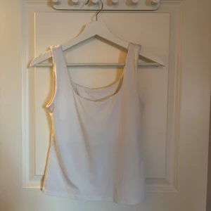 Vit  linnetopp - Säljer en enkel och stilren vit linnetopp med breda axelband och rundad halsringning. Toppen  en klassisk passform som funkar till det mesta. Perfekt att styla lager på lager eller bära som den är.