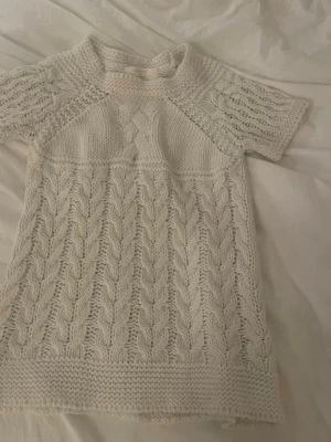 Vit kabelstickad topp från ZARA KNIT - Säljer en krämvit kabelstickad topp från ZARA KNIT med korta ärmar och rund hals. Tröjan har ett detaljerat flätmönster och är gjord i ett tjockare garn som ger en mysig känsla. Perfekt att styla med jeans eller kjol för en trendig look.
