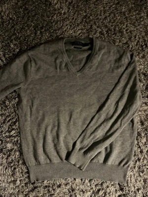 Grå stickad tröja från Polo Ralph Lauren🙌🤩 - Klassisk grå stickad tröja från Polo Ralph Lauren med V-ringning och diskret broderad logga på bröstet. Tillverkad i mjuk bomull och har ribbade muddar vid ärmslut och nederkant. Perfekt för lager på lager och enkel att matcha.🙌🤩