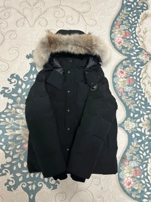 Svart dunjacka med pälskant från Canada Goose - Säljer en svart dunjacka från Canada Goose med stor huva och lyxig pälskant. Jackan har klassisk patch på ärmen, flera fickor och stängs med både dragkedja och knappar. Perfekt för kalla vinterdagar och riktigt snygg passform. Its never used with tags. 