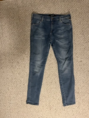 Replay blå slim jeans - Säljer ett par blå slim jeans från Replay med klassisk femficksdesign och snygga slitningar framtill. Jeansen har normal midja och smal passform hela vägen ner. Perfekta till sneakers eller boots och riktigt sköna tack vare stretchigt material. Hör av dig vid frågor om storlek