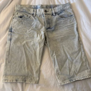Ljusblå jeansshorts i loose fit - Snygga ljusblå jeansshorts med klassisk femficksdesign och bälteshällor. Modellen är loose fit och går ner till knäna, perfekt för en avslappnad stil. Tillverkade i mjukt denimtyg med en ljus tvättad look.