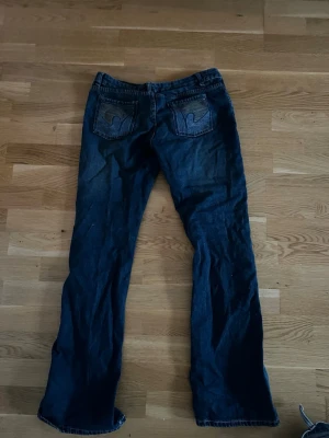 Mörkblå bootcut jeans  - Snygga mörkblå jeans med klassiska bakfickor och bootcut passform. Jeansen har en rak midja och är tillverkade i slitstarkt bomullsdenim. Perfekta för dig som gillar en tidlös och avslappnad stil.