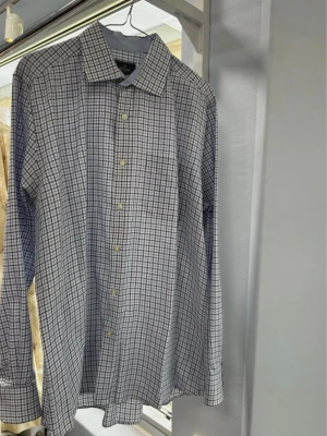 Rutig skjorta från Park Lane L - Klassisk rutig skjorta från Park Lane i storlek L. Skjortan är vit med blått rutmönster, har lång ärm, knappar framtill och en bröstficka. Tillverkad i mjuk bomull som känns skön mot huden. Perfekt till jeans eller chinos.