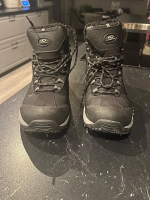 Svarta Icebug vinterkängor från Catmandoo - Svarta icebug kängor från Catmandoo med snörning och robust sula. Utsidan är i syntetmaterial och insidan är fodrad för extra värme. Perfekta för kalla dagar med sin höga modell och slitstarka design.