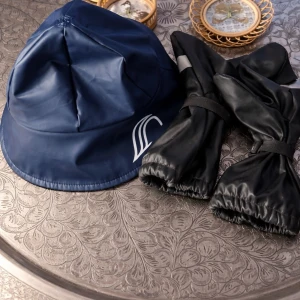 Fräsch Marinblå regnmössa   Äfrån Galon ett par tum   barn vantar   - Säljer en marinblå regnmössa ett par  mörka blå-svarta tumvantar  från Galon i vattentätt material. form med bred skärm och vitt tryck på sidan. Insidan har mjukt foder för extra komfort. Likadantmed vantarna har foder och är vattensäkra.  Snygg och funktionell accessoars gör kalla och snöiga dagar. 