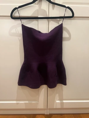 Mörklila tuptop Zara - Säljer en mörklila tubtop med peplumvolang nedtill. Toppen har en mjuk, sitter snyggt med en lätt utsvängd form. Perfekt att styla med jeans eller kjol för en trendig look.