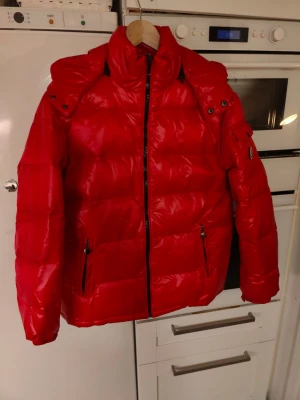 Ny oanvänd,  Röd pufferjacka med huva - Snygg röd pufferjacka med huva och hög krage. Jackan har dragkedja framtill och  Helt ny oanvänd. 
