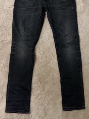 Mörkblå raka jeans från Nudie - Säljer ett par svarta jeans från Nudie med raka ben och klassisk femficksmodell. Jeansen har lite slitningar och kontrastsömmar som ger en snygg look. Storlek 30/30 men är rätt så långa ändå.