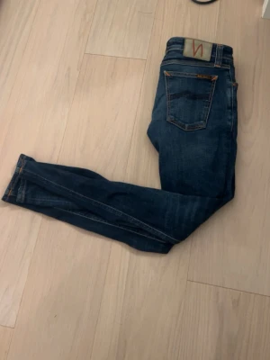 Mörkblå slim jeans från Nudie - Säljer ett par mörkblå slim jeans från Nudie med klassiska bakficka med Nudie-logga. Dem är knappt använda och är riktigt stilrena