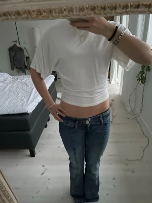 Vit croppad topp från 157 - Säljer en vit croppad topp från 157 med korta, vida ärmar och tight passform i midjan. Toppen är enkel och stilren, perfekt till jeans eller kjol. Tillverkad i mjuk bomull för en skön känsla.