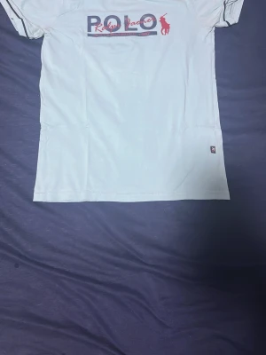 Vit Polo Ralph Lauren t-shirt - Snygg vit t-shirt från Polo Ralph Lauren med klassisk logga och röd häst på bröstet. T-shirten har korta ärmar och rund halsringning. Tillverkad i mjuk bomull för en skön känsla. Perfekt till jeans eller shorts för en clean look.