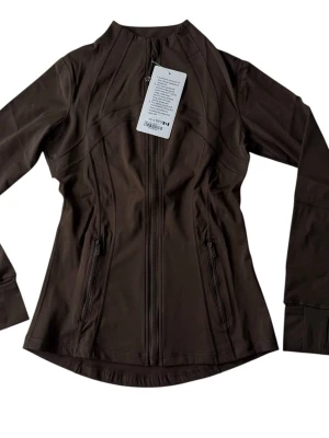 Brun tröja från Lululemon - Säljer denna Lululemon jacka i fin brun färg, helt ny/oanvänd med prislapp kvar. Perfekt för både träning, yoga, gym, löpning och vardag. Stilren design som passar året runt. Hög kvalitet, bekväm passform och exklusivt material. Storlek 4. Råkade riva av lappen inuti och blev ett litet hål, syns dock bara när man lyfter tyget. Därav det billiga priset.