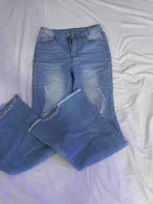 Ljusblå bootcut jeans med slitningar Shein  - Säljer ett par ljusblå jeans med bootcut-modell och slitna detaljer på benen. Jeansen har fransiga benslut och klassisk femficksdesign. Perfekta för dig som gillar en avslappnad och trendig look.