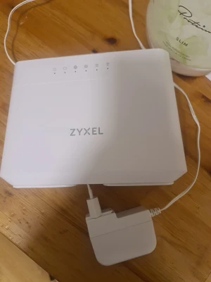 Vit router från Zyxel med adapter - Säljer en vit router från Zyxel med tillhörande strömadapter. Routern har en stilren, rektangulär design med flera statuslampor på ovansidan. Perfekt för att förbättra ditt wifi hemma eller på kontoret.